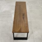 Träbänk med metallben på klinkergolv.