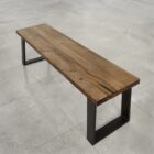 Träbänk med svarta metallben på stengolv.