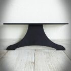 Svart metallfot på trägolv mot vit vägg.