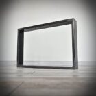 Metallram på trägolv mot vit vägg.